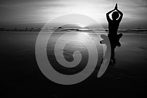 Young woman practicing yoga on the sea beach. Black and white high contrast photography.