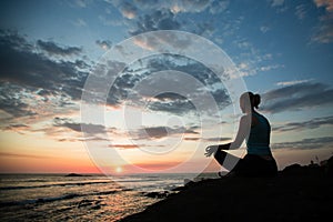 Young woman practicing yoga sitting in Lotus position on the ocean coast