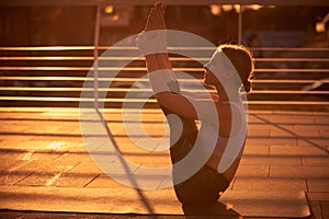 Young woman practicing yoga, sitting in Paripurna Navasana exercise in the terrace at sunset