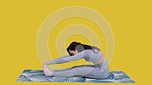 Young woman practicing yoga while sitting on yoga mat on the yellow chroma key