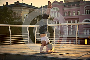 Young woman practicing yoga, standing in Pincha Mayurasana - Forearm stand in the terrace at sunset