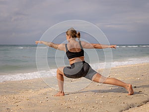 Young woman practicing yoga. Standing in Virabhadrasana II pose, Warrior II Pose. Work out. Healthy lifestyle. Strong body. Ocean