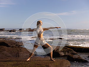 Young woman practicing yoga. Standing in Virabhadrasana II pose, Warrior II Pose. Work out. Healthy lifestyle. Strong body. Ocean