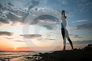 A young woman practicing yoga during sunset on the seashore. Relax.