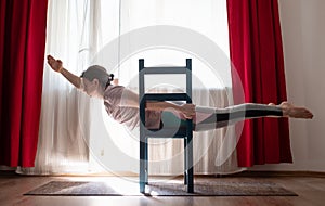 Young woman practicing yoga in Superman Pose or Viparita Shalabhasana using chair