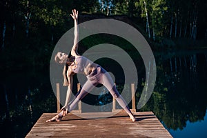 Young Woman practicing yoga on the wooden berth at lake. Single sport healthy training on nature at sunny weather