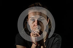 Young woman praying to god with prayer beads with a crucifix on the cross