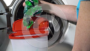 Young woman prepare to wash clothes in washing machine and takes out and opens box with washing powder with laundry