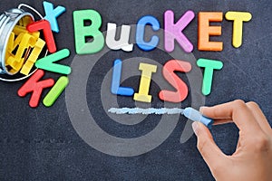 Young woman prepared for bucket list with metallic bucket and colorful plastic letters on blackboard