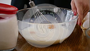 Young woman prepares dough mixing ingredients in the the bowl using whisk in the kitchen. Homemade food. Slowmotion shot