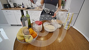 Young woman prepares dough mixing ingredients in the the bowl using whisk in the kitchen. Homemade food. Slowmotion shot