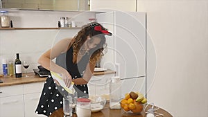 Young woman prepares dough mixing ingredients in the the bowl using whisk in the kitchen. Homemade food. Slowmotion shot