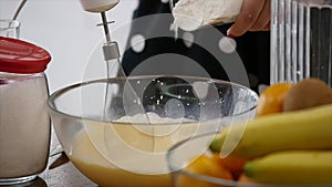 Young woman prepares dough mixing ingredients in the the bowl using whisk in the kitchen. Homemade food. Slowmotion shot