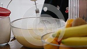 Young woman prepares dough mixing ingredients in the the bowl using whisk in the kitchen. Homemade food. Slowmotion shot