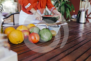 young woman preparing a healthy recipe of diverse fruits, watermelon, orange and blackberries. Using a mixer. Homemade, indoors,