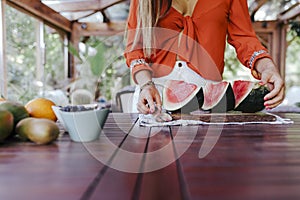 young woman preparing a healthy recipe of diverse fruits, watermelon, orange and blackberries. Using a mixer. Homemade, indoors,