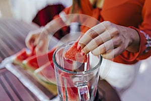 young woman preparing a healthy recipe of diverse fruits, watermelon, orange and blackberries. Using a mixer. Homemade, indoors,