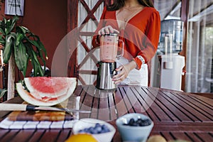 young woman preparing a healthy recipe of diverse fruits, watermelon, orange and blackberries. Using a mixer. Homemade, indoors,