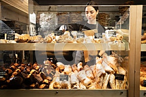 Young woman preparing pastry for sale in supermarket bakery department. Bakery seller.