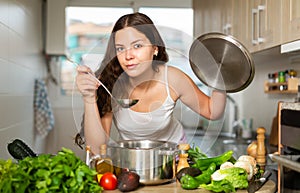 Young woman preparing soup in saucepan in kitchen