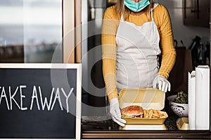 Young woman preparing take away fast food inside kitchen restaurant - Focus on hands holding burger