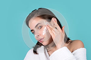 Young woman preparing to start her day, applying moisturizer cream on face. Beautiful girl model with natural makeup.