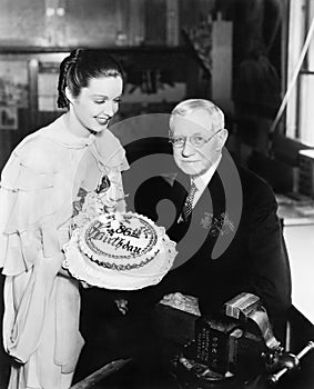 Young woman presenting a birthday cake to an elderly man