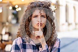 Young woman presses finger to lips makes silence hush sign do not tells gossip secret quiet in city