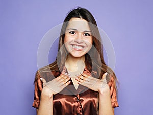 Young woman presses her hands to her chest, feels surprised over purple background