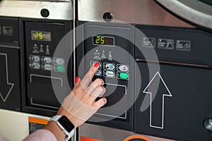 Young woman pressing button in washing machine at public laundry.