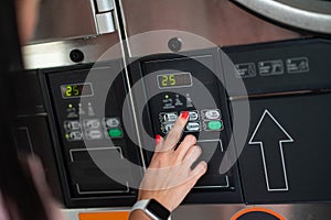 Young woman pressing button in washing machine at public laundry.