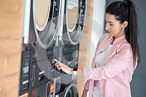 Young woman pressing button in washing machine at public laundry.