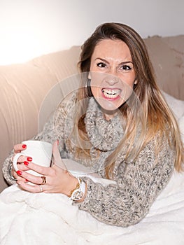 Young woman pretends to growl sitting on home couch in house drinking tea hot drink coffee in winter day photo