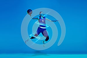 Young woman professional basketball player in jump isolated on blue studio background in neon light with geometric