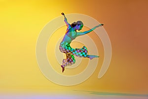 Young woman, professional contemporary dancer in motion, in stylish clothes against gradient yellow orange background in