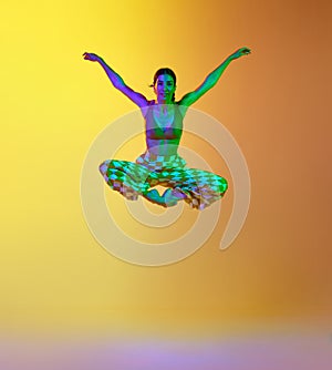Young woman, professional contemporary dancer in motion, in stylish clothes against gradient yellow orange background in