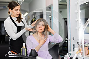 Young woman professional hair stylist choosing hairdo for female client