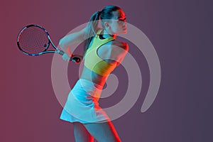 Young woman, professional tennis player training isolated on blue background in neon.