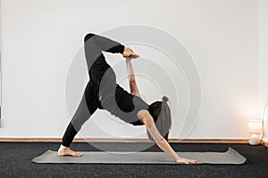 Young woman professional trainer in black sportswear stretching muscles indoors. Sporty girl is doing stretching or yoga. Healthy