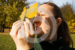 Young woman in profile with yellow leaves, sunlight, shadows, hands close up, autumn inspiration