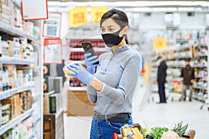 Young woman in protective mask and gloves scanning a barcode of a product while shopping in a supermarket