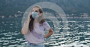 A young woman in a protective mask is talking on the phone. View of the bay and the grps. Portrait of a woman in a