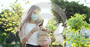 Young woman in protective mask using smartphone in the park. Worried girl searching news about Covid-19. Pandemic Covid