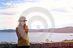 Young woman with a protective mask using a smartphone on vacation in a lookout point.