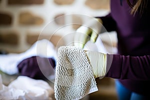 Young woman in protective rubber gloves cleaning bright light-toned tiled wall at home