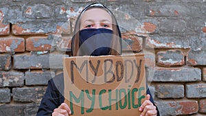 Young woman protester holds cardboard with MY BODY MY CHOICE sign shows middle finger. Girl protesting against anti-abortion laws.