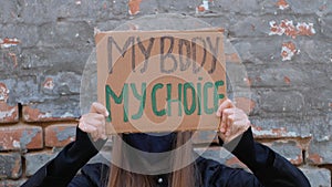 Young woman protester holds cardboard with MY BODY MY CHOICE sign shows middle finger. Girl protesting against anti-abortion laws.