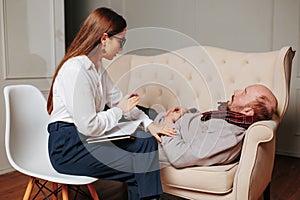 Young woman psychologist calms elderly client during psychotherapeutic session in office.