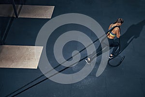 Young woman pulling rope at gym turning back