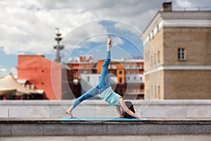 Young woman pulls a leg up in front urban buildings